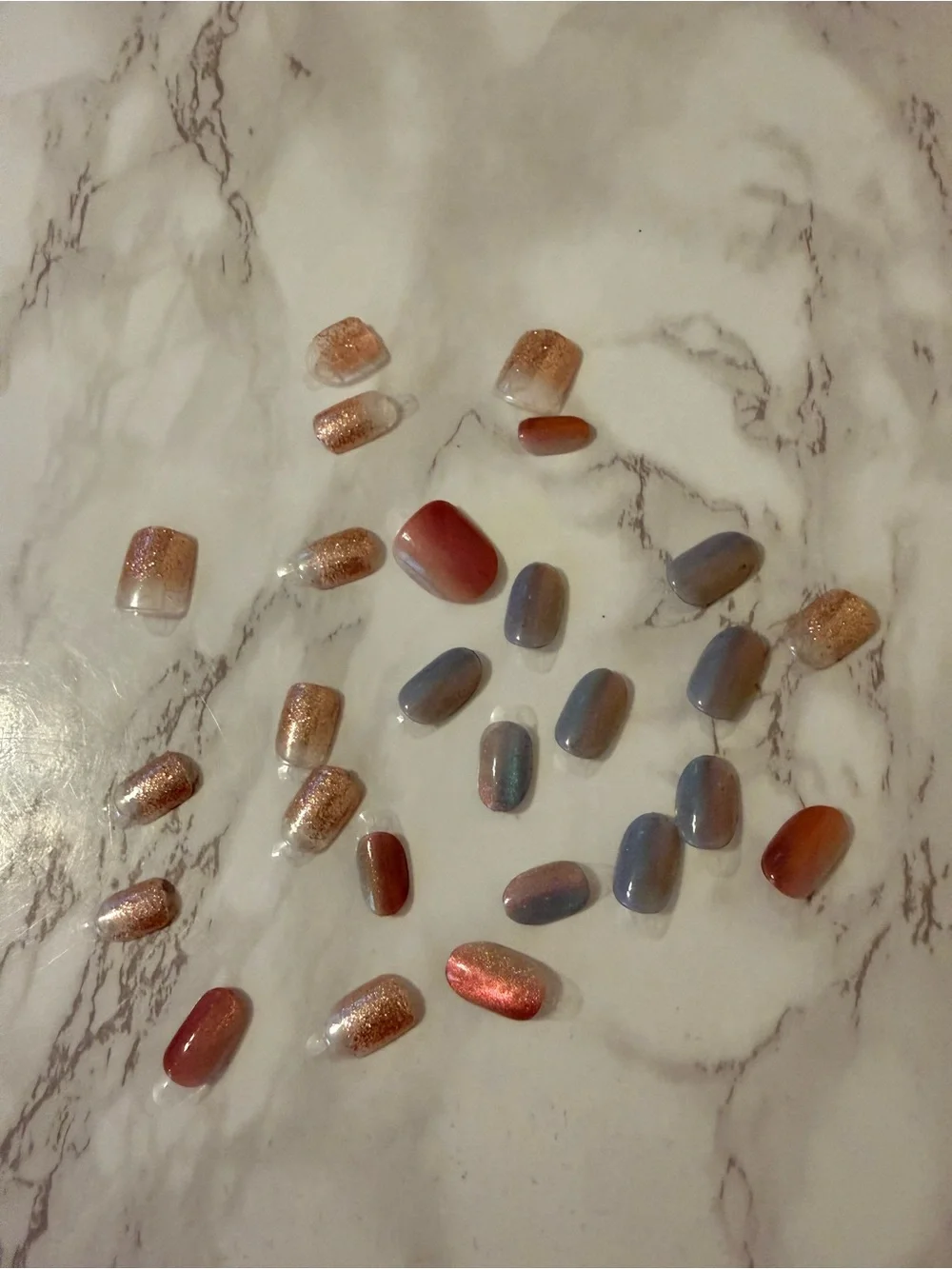 Assorted Press-On Nail Set in Rose Gold, Coral, and Blue with black pouch.